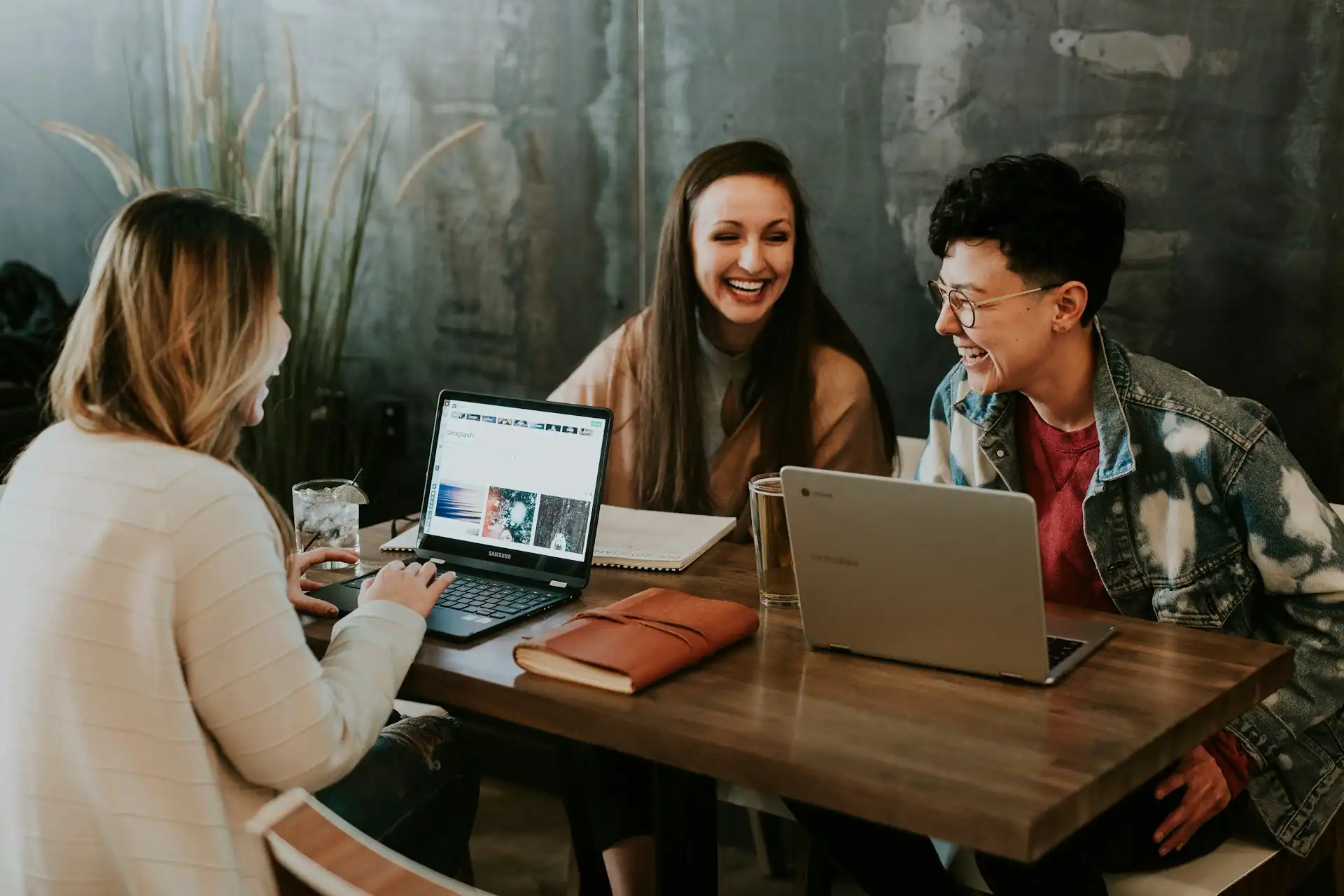 Three students sitting in front of table laughing together